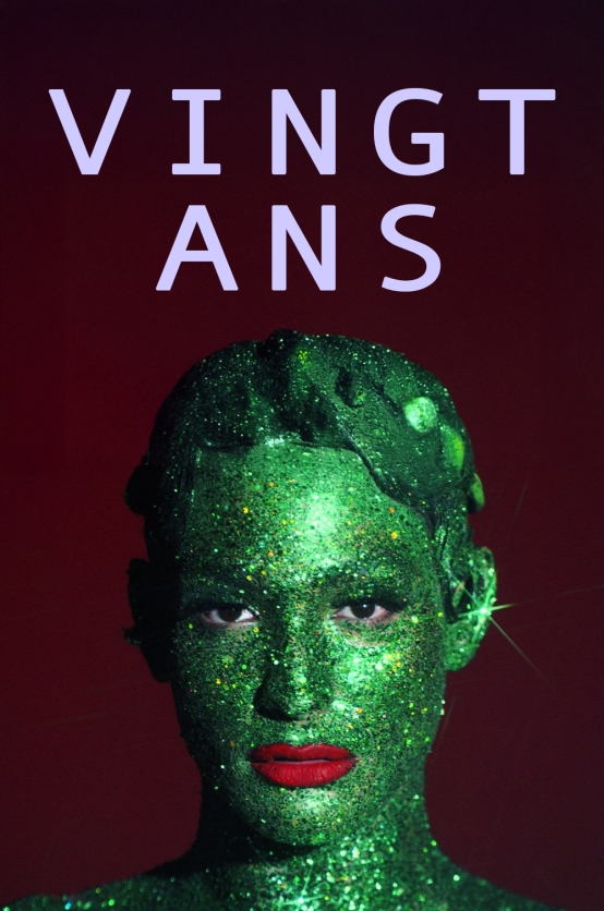 Vingt Ans L'image montre un portrait centré d'une personne maquillée avec une peau entièrement recouverte de paillettes vertes brillantes. Ses yeux regardent droit vers l'objectif avec une expression intense. Elle porte un rouge à lèvres rouge vif qui contraste fortement avec la teinte verte de sa peau. L'arrière-plan est sombre, légèrement rouge. Un texte en lettres majuscules, "VINGT ANS", est positionné en haut de l'image, de couleur violette claire avec une police épurée.