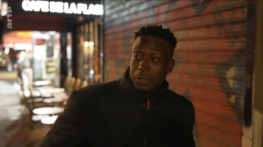 On voit un jeune homme dans la rue, devant le 'café de la place'