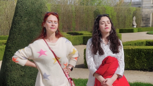 Inès et sa mère se tiennent côte à côte dans le jardin de Versailles. Elles ferment toutes les deux les yeux et ont des expressions fermées, entre la sérénité et la tristesse. 