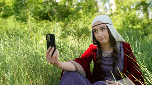 On voit la comédienne déguisée en Iseut qui est assise dans une clairière et qui semble prendre un selfie.